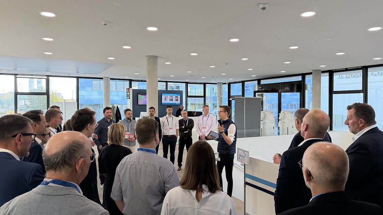 Automation Next Conference 2026 - Die Bosch Rexroth Werksführung hat gestartet, Teilnehmer hören sich den Vortrag an und schauen Richtung Speaker